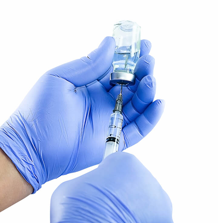 A pair of hands in blue latex gloves filling a syringe from a glass medicine vial