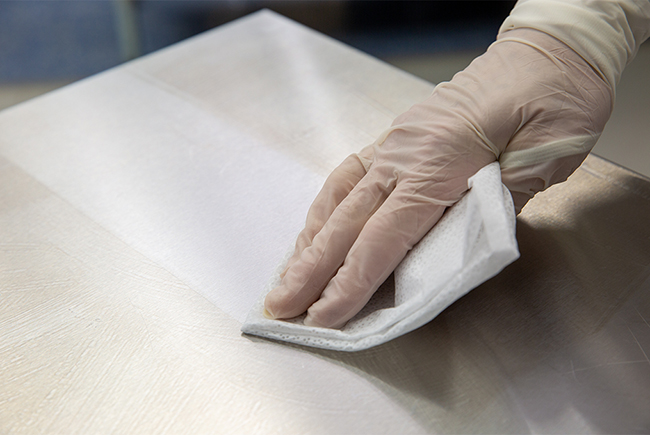 A gloved hand using an antiseptic wipe on a stainless steel surface