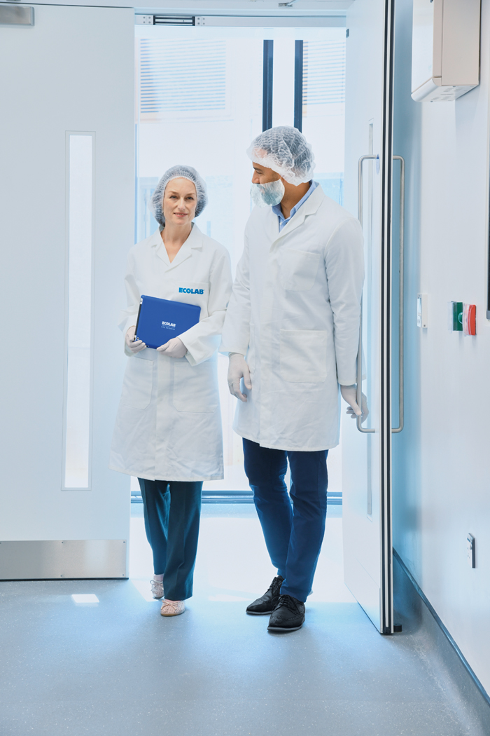 Two scientists in lab coats and hair nets walking together down a hall