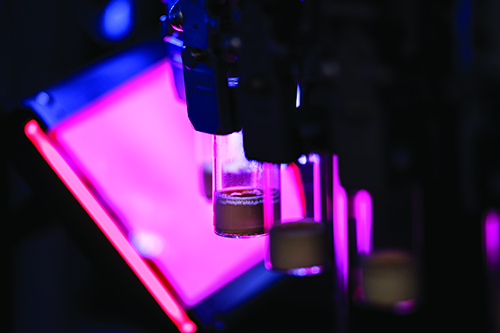 Various medicine vials in an automated process being scanned against a purple/magenta light